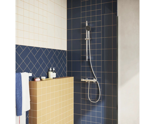 Moderne Dusche mit verchromtem Duschset auf dunkelblauen Fliesen, gelber Ablage und blauem Fischgrät-Fliesenmuster.