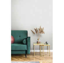 Modernes Wohnzimmer mit grünem Samtsofa und goldenen Satztischen. Eine Vase mit getrocknetem Pampasgras steht auf dem Tisch vor hellen Tapeten.