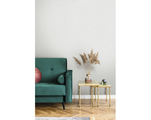 Modernes Wohnzimmer mit grünem Samtsofa und goldenen Satztischen. Eine Vase mit getrocknetem Pampasgras steht auf dem Tisch vor hellen Tapeten.