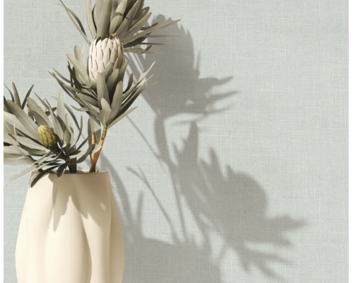 Strukturierte Tapete in Leinenoptik an einer Wand mit einer Vase mit Trockenblumen und Schattenwurf.