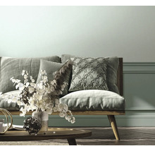 Helles Wohnzimmer mit einem Sofa aus Holz, gemusterten Kissen, einem Couchtisch aus Holz und einer Wand mit Zierleisten.