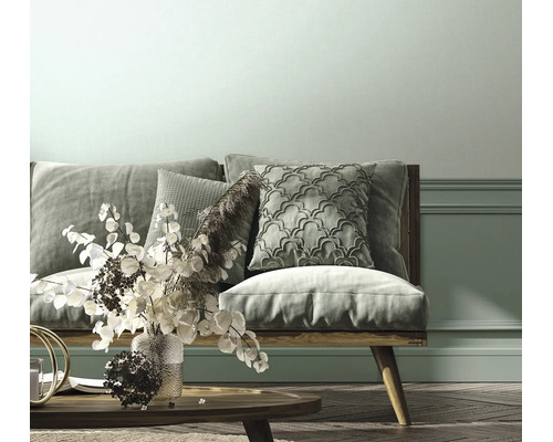 Helles Wohnzimmer mit einem Sofa aus Holz, gemusterten Kissen, einem Couchtisch aus Holz und einer Wand mit Zierleisten.