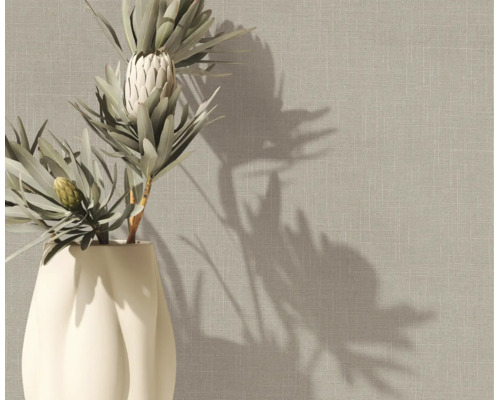 Vliestapete mit Leinenstruktur in Beige an einer Wand hinter einer Vase mit Protea-Blumen.