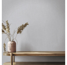 Vliestapete in Leinenoptik an einer Wand hinter einer Vase mit Trockenblumen auf einer Holzbank.
