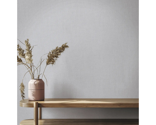 Vliestapete in Leinenoptik an einer Wand hinter einer Vase mit Trockenblumen auf einer Holzbank.