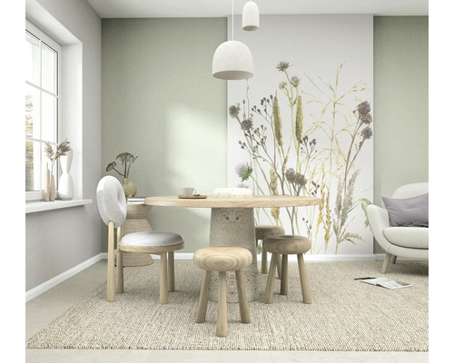 Helles Esszimmer mit einer Vliestapete mit Gräsern und Disteln, rundem Holztisch und Sitzmöbeln aus Holz auf einem Teppich.