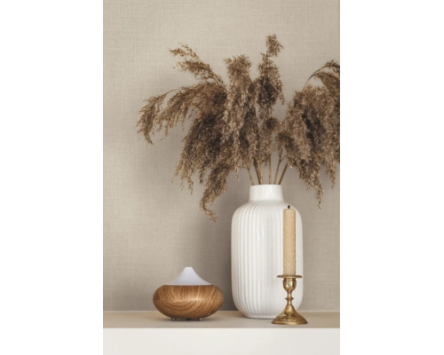 Strukturierte beige Tapete in Leinenoptik hinter einer weißen geriffelten Vase mit Trockengras, einem Aroma-Diffuser und einem Kerzenständer.