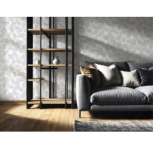 Vliestapete mit Ginkgo Blattmuster in einem hellen Wohnzimmer mit Sofa und Regal aus Holz und Metall auf einem Holzboden.