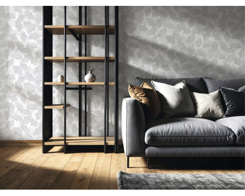 Vliestapete mit Ginkgo Blattmuster in einem hellen Wohnzimmer mit Sofa und Regal aus Holz und Metall auf einem Holzboden.