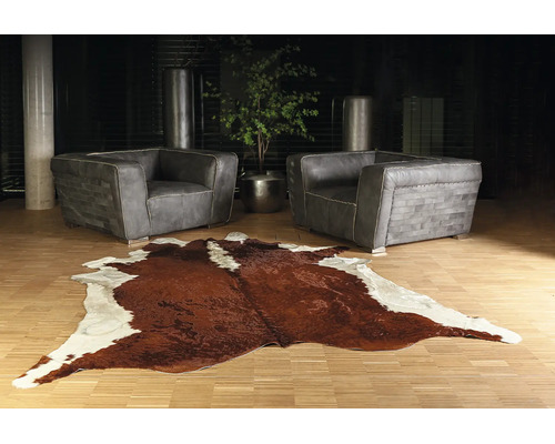 Modernes Wohnzimmer mit zwei grauen Ledersesseln und einem braun-weißen Kuhfellteppich auf hellem Holzfußboden.