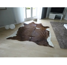 Naturgeformter Teppich aus Kuhfell in einem hellen, modern eingerichteten Wohnzimmer mit hellem Parkettboden.