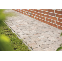 Gepflasterter Gartenweg aus rechteckigen Steinen zwischen einer Ziegelwand und einer Rasenfläche.