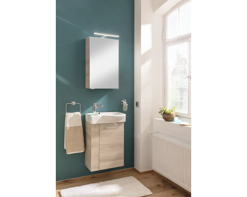 Modernes Gäste-WC mit hellem Waschtischunterschrank aus Holz, weißem Keramikwaschbecken, Spiegelschrank mit Beleuchtung und Handtuchhalter.