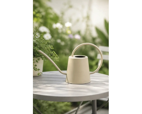 Beige Gießkanne aus Metall mit langem Ausguss und rundem Griff auf einem Gartentisch.
