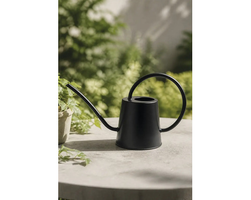 Schwarze Gießkanne aus Metall mit langem Auslauf und kreisförmigem Griff auf einem Tisch.