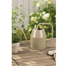 Moderne Metallgießkanne auf einem Holztisch im Garten mit kleiner Pflanze und Gartenhandschuhen in einer hellen Atmosphäre.