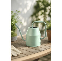 Moderne Gießkanne aus Metall in Mintgrün auf einem Holztisch mit Pflanzen und Gartenhandschuhen.