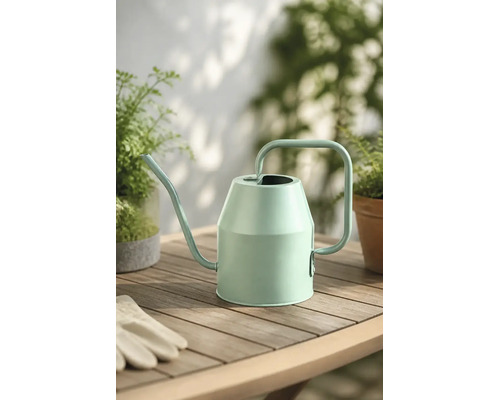 Moderne Gießkanne aus Metall in Mintgrün auf einem Holztisch mit Pflanzen und Gartenhandschuhen.