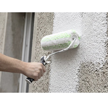 Eine Hand streicht eine grob strukturierte Fassade mit einer Fassadenrolle.