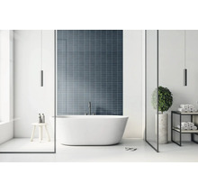 Modernes, helles Badezimmer mit freistehender Badewanne vor einer dunkelblauen Wand aus rechteckigen Mosaikfliesen.