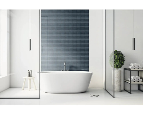 Modernes, helles Badezimmer mit freistehender Badewanne vor einer dunkelblauen Wand aus rechteckigen Mosaikfliesen.