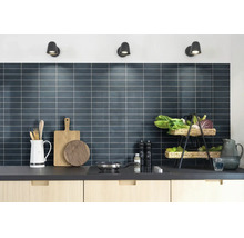 Moderne Küche mit dunklem Fliesenspiegel, hellen Holzschränken und Küchenutensilien unter drei Wandstrahlern.