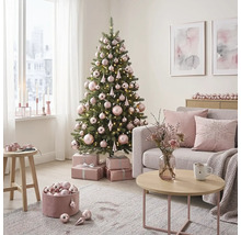 Hell eingerichtetes Wohnzimmer mit geschmücktem Weihnachtsbaum, rosa Christbaumkugeln, Geschenken, Sofa mit Kissen und Couchtisch.