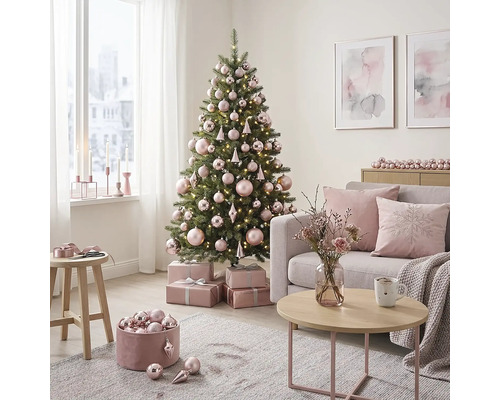 Hell eingerichtetes Wohnzimmer mit geschmücktem Weihnachtsbaum, rosa Christbaumkugeln, Geschenken, Sofa mit Kissen und Couchtisch.