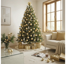 Festlich geschmückter künstlicher Weihnachtsbaum mit warmweißen Lichtern und goldenen Kugeln in einem hellen Wohnzimmer mit Sofa und Geschenken.