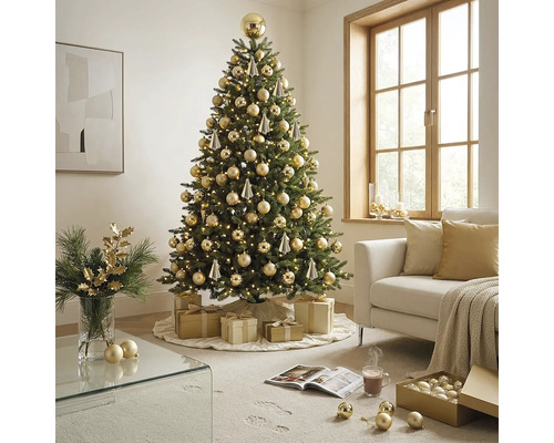 Festlich geschmückter künstlicher Weihnachtsbaum mit warmweißen Lichtern und goldenen Kugeln in einem hellen Wohnzimmer mit Sofa und Geschenken.
