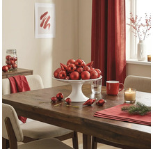 Festlich gedeckter Holztisch mit einer weißen Etagere voller roter Christbaumkugeln, einer Kerze und Adventsdekoration.