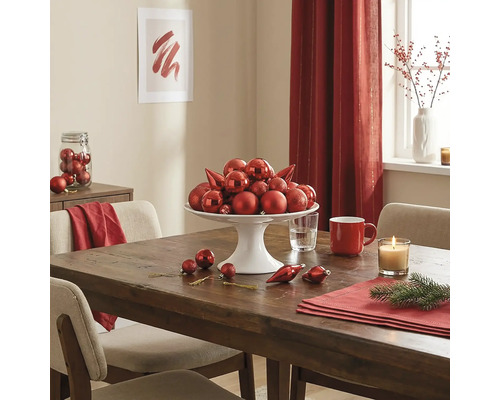 Festlich gedeckter Holztisch mit einer weißen Etagere voller roter Christbaumkugeln, einer Kerze und Adventsdekoration.