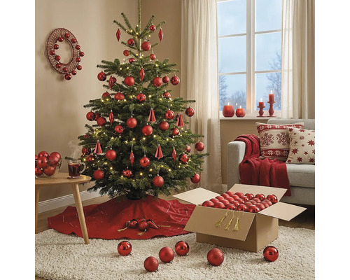 Festlich geschmückter Weihnachtsbaum mit roten Kugeln und LED-Lichterkette in einem wohnlichen Zimmer mit Sofa und Weihnachtsdekoration.