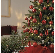 Weihnachtsbaum geschmückt mit verschiedenen roten Ornamenten und warmweißen Lichtern in einem hellen Wohnzimmer.