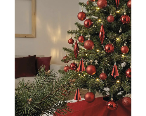 Weihnachtsbaum geschmückt mit verschiedenen roten Ornamenten und warmweißen Lichtern in einem hellen Wohnzimmer.