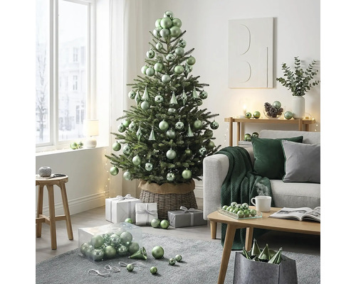 Hell dekorierter Wohnraum mit Christbaum in einem Weidenkorb, geschmückt mit Kugeln. Daneben Sofa, Couchtisch und Geschenke.