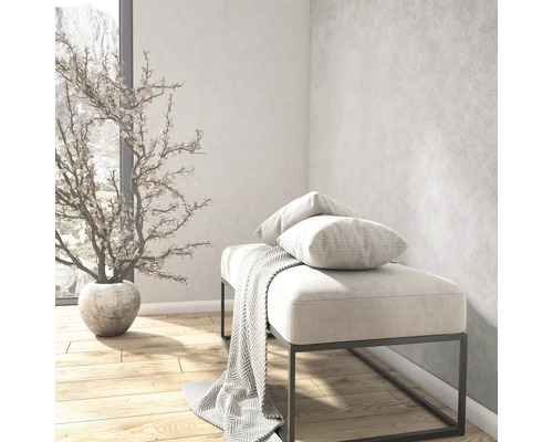 Heller, organisierter Raum mit strukturierter Wandgestaltung, einer Bank mit Metallgestell, Kissen und Decke sowie einem Dekobaum auf Holzboden.