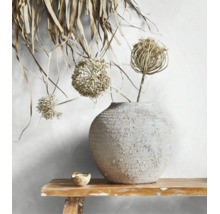 Runde Keramikvase mit rauer Textur und getrockneten Blüten auf einer Holzbank vor einer hellen Wand.