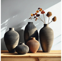 Arrangement von fünf strukturierten Keramikvasen in verschiedenen Formen und Erdtönen auf einer Holzoberfläche, mit Trockenblumen in einer Vase.