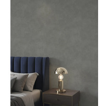 Schlafzimmer mit dunkelgrau strukturierter Wand, blauem Samtkopfteil und goldfarbener Tischleuchte auf einem Nachttisch.