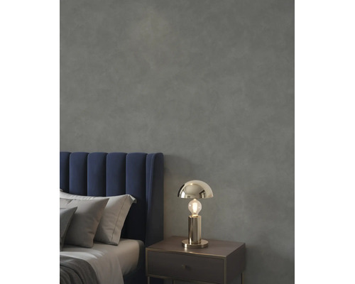Schlafzimmer mit dunkelgrau strukturierter Wand, blauem Samtkopfteil und goldfarbener Tischleuchte auf einem Nachttisch.
