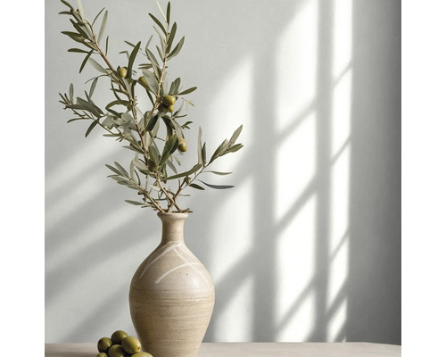 Olivenzweig mit Oliven in einer dekorativen Keramikvase in einem hellen Raum mit Lichteinfall und Schatten.