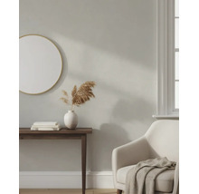Hell gestalteter Wohnraum mit beige gestrichener Wand, rundem Spiegel, dunklem Konsolentisch, weißer Vase und bequemem Sessel.
