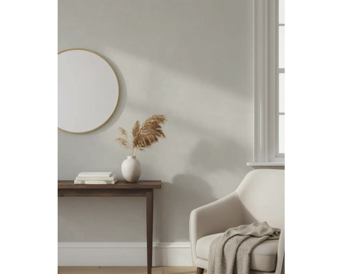 Hell gestalteter Wohnraum mit beige gestrichener Wand, rundem Spiegel, dunklem Konsolentisch, weißer Vase und bequemem Sessel.