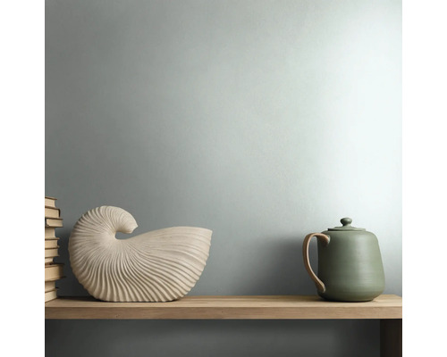 Modernes Zimmer mit mattgrün gestrichener Wand, Holzregal, skulpturalem Deko-Objekt in Muschelform und grüner Keramik-Teekanne.