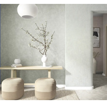 Hell gestalteter Raum mit strukturierter Wand, hölzerner Konsole, zwei geflochtenen Sitzhockern, Teppich und Vase mit Zweigen.