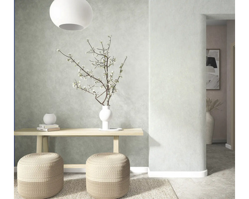 Hell gestalteter Raum mit strukturierter Wand, hölzerner Konsole, zwei geflochtenen Sitzhockern, Teppich und Vase mit Zweigen.