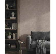 Modernes Wohnzimmer mit strukturierter rosa Wand, dunkelgrünem Samtsofa und einem dunklen Holzregal mit Büchern und Dekoration.