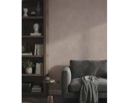 Modernes Wohnzimmer mit strukturierter rosa Wand, dunkelgrünem Samtsofa und einem dunklen Holzregal mit Büchern und Dekoration.