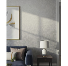 Modernes Wohnzimmer mit grauer Strukturtapete mit dezentem geometrischem Muster, blauem Sofa, Beistelltisch und Lampe.